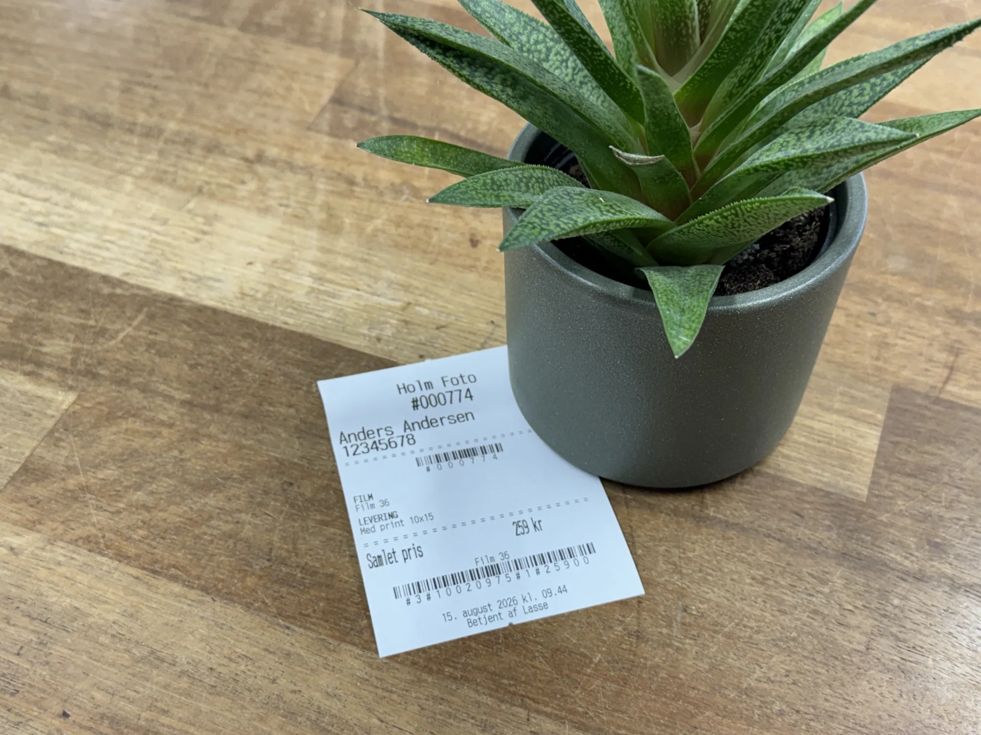 The receipt is printed directly from the system via PrintNode to the shop's Epson thermal printer. It includes the order number, customer name and phone number, a full itemised breakdown of all selected products and prices, the start-up fee, and the total amount due. For film and negative orders, a Code128 barcode containing the order number is added at the top, allowing the lab to scan the order straight into their workflow. At the bottom, dynamic C1st barcodes are generated for each product, which the staff menber scans directly into the point-of-sale system — eliminating the need to manually key in any items or prices.